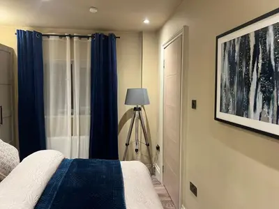 a bedroom with a bed with blue curtains and a lamp at 2 bedroom self catering detached outhouse with garden area in Preston