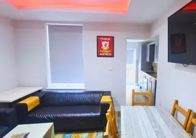 a living room with a black leather couch and a table at The Red Lounge House Near Anfield sleeps 14 LFC in Liverpool