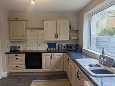 a kitchen with wooden cabinets and a sink and a window at STANLEY HOUSE MORECAMBE Modern spacious 3 bed family home near seafront in Heysham