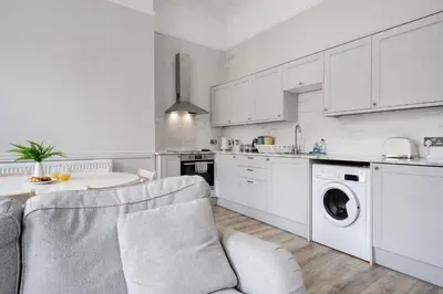 a kitchen with white cabinets and a table and a chair at Central L1 Stay, Close to all Attractions, Parking Nearby in Liverpool