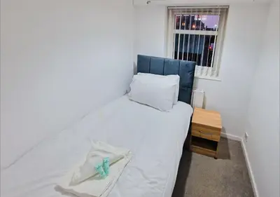 a small bedroom with a bed with a blue headboard and a window at Amazing Spacious 3BDR Home Near LFC Stadium in Liverpool