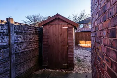 a wooden outhouse in a yard next to a brick fence at Cosy & Stylish Home in St Helens