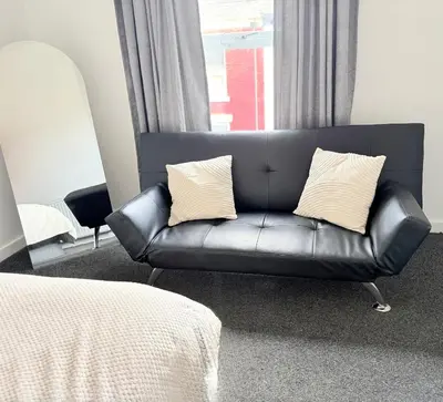 a black leather couch in a room with a window at Deepdale House - Comfortable 2 Bedroom Home near Major Attractions in Preston in Preston