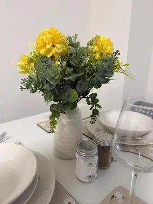 a vase with yellow flowers on a table with plates at City-Close Studio By Escape & Estates Short Lets & Serviced Accommodation Liverpool with Free parking and Wifi in Liverpool