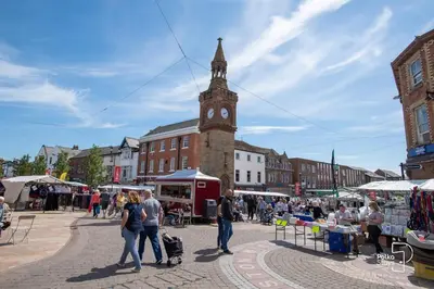 a group of people walking around a market with a clock tower at Comfy Ormskirk Family Stay by PolkaStays in Ormskirk