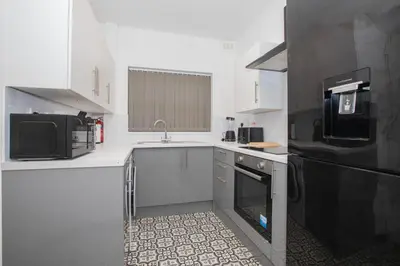 a kitchen with white cabinets and a black refrigerator at Cozy Liverpool Base Close to City Centre in Liverpool