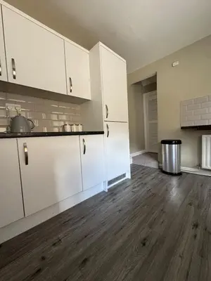 an empty kitchen with white cabinets and a wooden floor at Homely 3 bedroom House in Liverpool in Liverpool