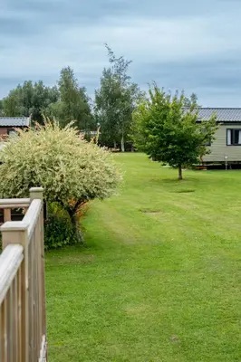 a yard with a fence and trees and a house at Blue Water Retreats in Carnforth