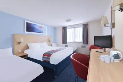 a hotel room with two beds and a chair at Travelodge Barrow In Furness in Barrow in Furness