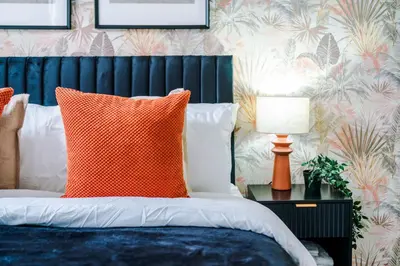 a bed with an orange pillow and a table with a lamp at Modern 3BR House in Liverpool - Garden in Liverpool
