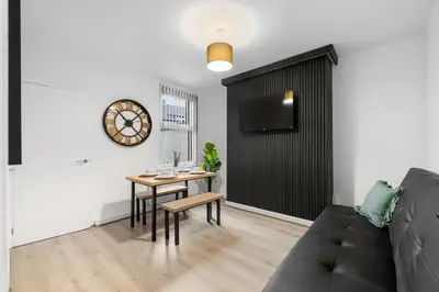 a living room with a table and a clock on the wall at Large 4BR House - Sleeps 7 - Long Stays Great Location in Litherland