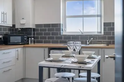 a white kitchen with a table with glasses and plates at 2BR Flat - 4 Beds Sleeps 7 - Trinity Vaults in Liverpool