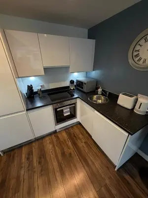 a kitchen with white cabinets and a clock on the wall at City View Studio Apartment Liverpool by StaySavvy Accommodation in Liverpool