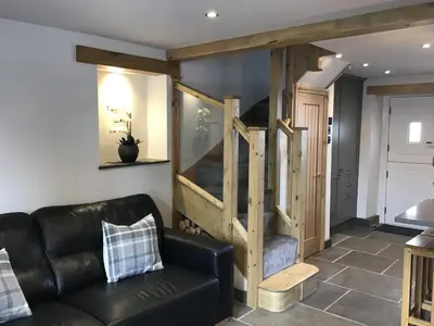 a living room with a black leather couch and a staircase at Tastefully Renovated Cottage in Ulverston in Ulverston