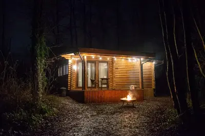 a small cabin in the woods at night at Log cabin in private woodland with lake in Borwick