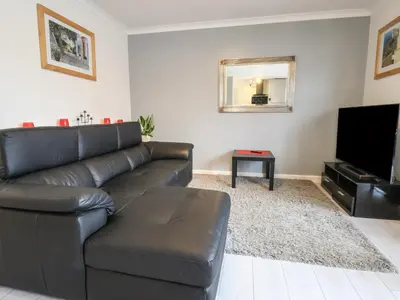 a living room with a black leather couch and a flat screen tv at Flat 12 in Wallasey