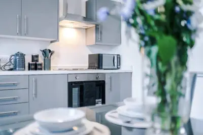 a kitchen with white appliances and a table with dishes at 3-BR Home in Wigan | Free Wi-Fi | Comfortable Stay in Ince-in-Makerfield