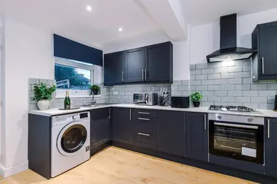 a kitchen with black cabinets and a washer and dryer at Comfy 3-BR Wirral Home | Free Parking & Wi-Fi in Bidston