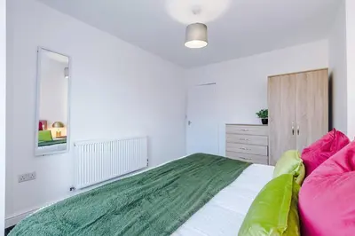 a bedroom with a large bed with pink and green pillows at Comfy 3-BR Wirral Home | Free Parking & Wi-Fi in Bidston