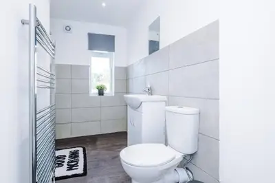 a white bathroom with a toilet and a window at Comfy 3-BR Wirral Home | Free Parking & Wi-Fi in Bidston