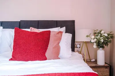 a bed with red pillows and a vase of flowers at Cozy 2BR Flat in the Heart of Wigan Wallgate in Wigan