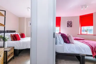 two beds in a room with red curtains at Cozy 2BR Flat in the Heart of Wigan Wallgate in Wigan