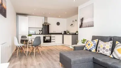 a living room with a grey couch and a kitchen at Modern 2BR Near Liverpool ONE & Parking in Liverpool