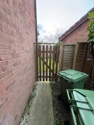 a green trash can sitting next to a brick wall at 1 Bed Apartment With Private Garden in Southport