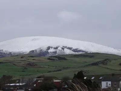 a snow covered mountain on top of a green field at Seaview Cottage Lake District Coast in Millom