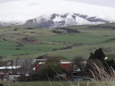 a snow covered mountain in a green field at Seaview Cottage Lake District Coast in Millom