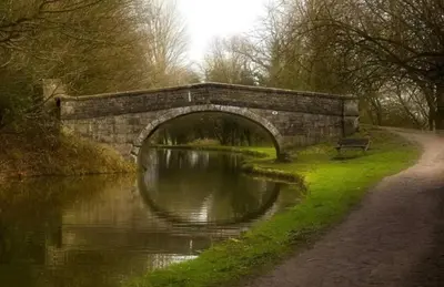 a stone bridge over a river with a bench at Cosy Parbold Apartment Steps form train station in Parbold