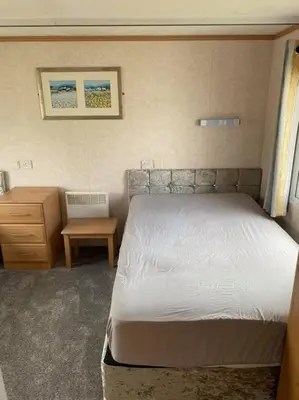 a bedroom with a white bed and a nightstand and a bed sidx sidx sidx at Spacious Caravan Morecambe Parkdean caravan Park in Morecambe