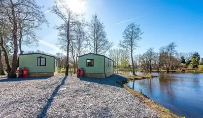 two green houses sitting on the side of a river at Bowland Lakes Leisure Village in Forton