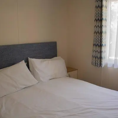 a bed with white sheets and pillows next to a window at Bowland Lakes Leisure Village in Forton