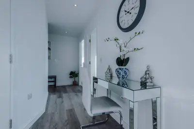 a white hallway with a table and a clock on the wall at Luxurious 2Bed Apartment, Sleeps 6, 3 beds in Preston