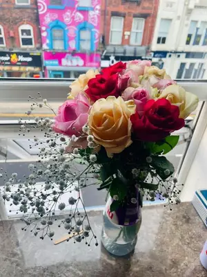 a vase with a bouquet of roses in a window at Cozy Cottage in Liverpool