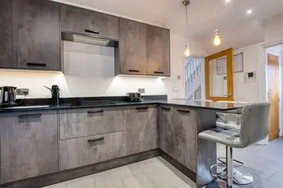 a kitchen with wooden cabinets and a bar with a stool at Westhoughton 3 Bedroom House - Free Parking in Westhoughton