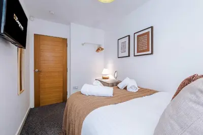 a bedroom with a bed with white sheets and a television at Centrally Located Formby Flat by 53 Degrees Property, Perfect for Work & Leisure in Formby