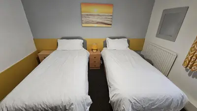 two beds in a small room with white sheets at Bowies Lodge in Blackpool