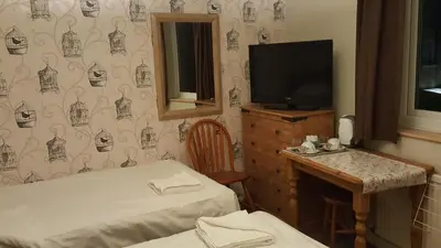 a room with two beds and a television and a table at Maindee Guest House in Barrow in Furness