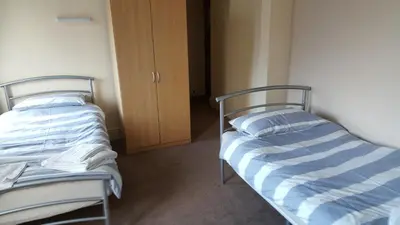 two twin beds in a room with a closet at The Lodge Guest Accommodation in Barrow in Furness