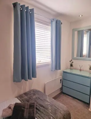a bedroom with blue curtains and a bed and a window at Fenna Lakeside Lodge - Pine Lake Resort in Carnforth