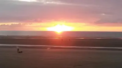 a sunset at the beach with people walking on the beach at MyRoomz Orchid Hotel in Blackpool