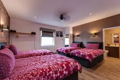 a bedroom with three beds with pink sheets and a couch at Tom Thumb Apartments in Liverpool