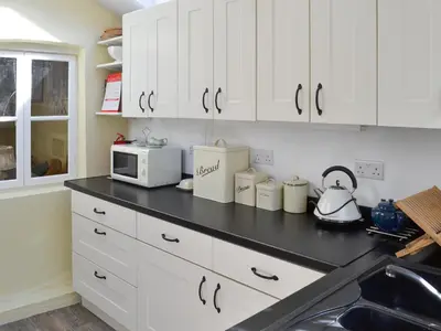 a kitchen with white cabinets and a black counter top at Woodburn Cottage in Soutergate