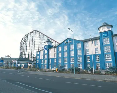 a large blue building with a roller coaster in the background at The Big Blue Hotel - Blackpool Pleasure Beach in Blackpool
