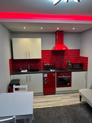 a kitchen with white cabinets and a red wall at Blackpool Beach Holiday Flats in Blackpool