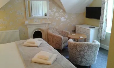 a room with a table and a chair and a fireplace at Elton Guest House in Grange Over Sands