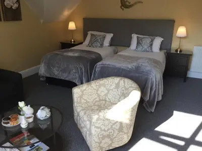 a hotel room with two beds and a chair at Elton Guest House in Grange Over Sands