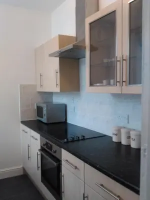 a kitchen with white cabinets and a black counter top at Delamere holiday flat in Blackpool